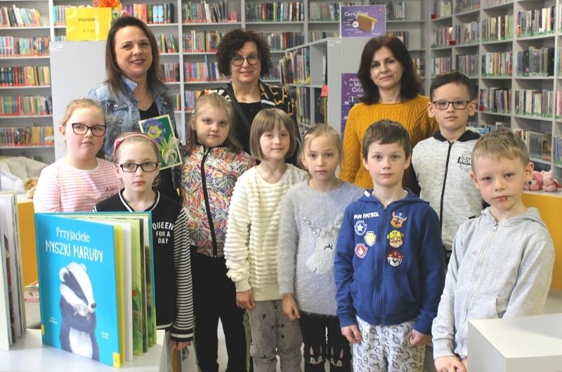 Na zdjęciu grupa dzieci wraz z opiekunem, bibliotekarką oraz dyrektorem biblioteki w Oddziale dla dzieci i młodzieży